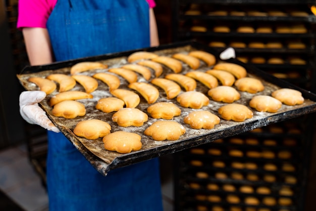 Tray with hot backed cookies. Factory for sweets production. Woman worker with fresh biscuit.