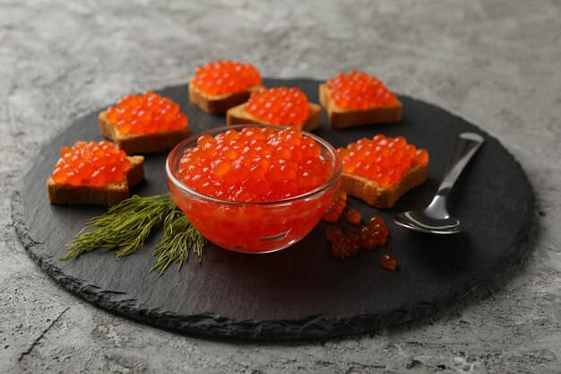 Foto vassoio con snack e ciotola con caviale rosso su grigio