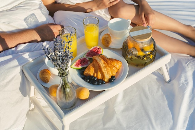 Tray with tea croissants in a white bed of a man and a woman on a cliff overlooking the sea at dawn