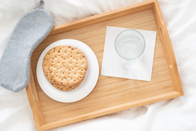 Tray with water and crackers dibreakfast on a bed