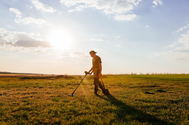 Treasure hunter stands against the blue sky Treasure hunter holding a modern metal detector Guy with a shovel looking for treasure