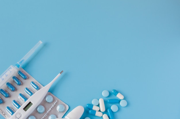 Treatment of colds and flu. Various medicines, a thermometer, sprays from a stuffy nose and a pain in a throat on a blue background. Copy space. Medicine flat lay