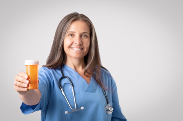 Treatment with pills happy senior doctor woman in uniform showing jar of medicines gray background