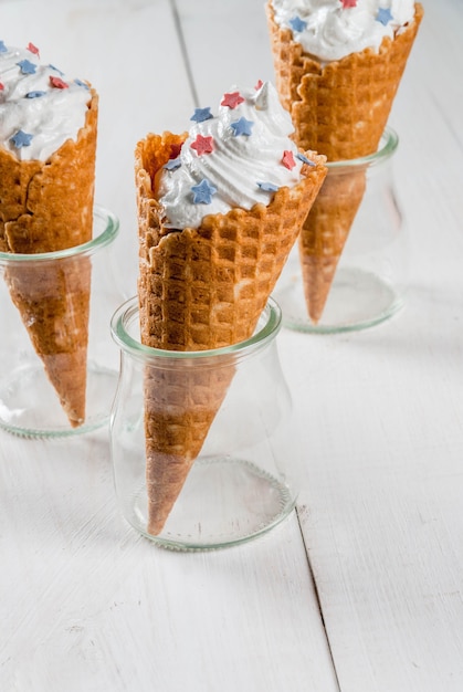 Фото Удовольствия к празднику дня независимости 4 июля домашнее кремовое мороженое в вафлях, украшенных звездами в традиционных цветах - на белом деревянном столе