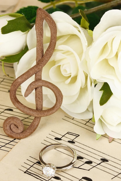 Скрипичный ключ, розы и обручальное кольцо на музыкальном фоне