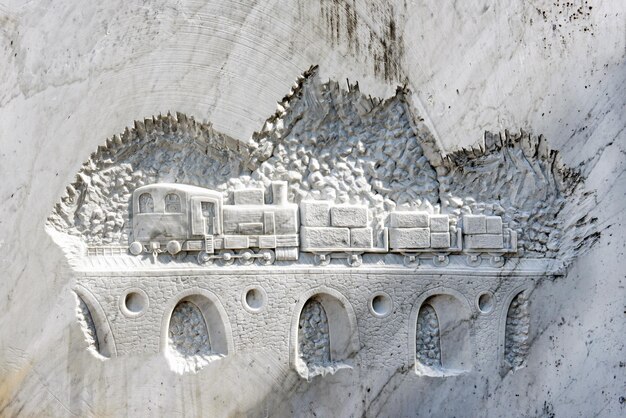 Foto trein met vracht rijden op gewelfde spoorbrug gesneden op witte marmeren muur