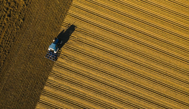 trekker die een veld ploegt. Industriële achtergrond op agrarisch thema. Gebruik drones om uw bedrijf te inspecteren.