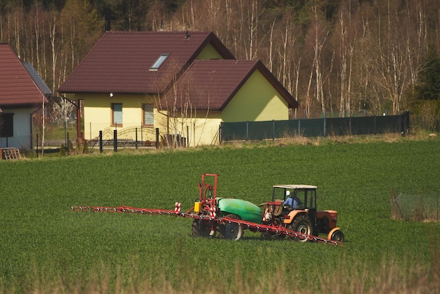 Trekker die pesticiden op het veld sproeit met een sproeier op landbouwvelden in het voorjaar in het lenteconcept van het platteland van de boerderij