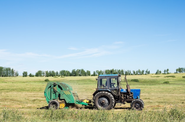 Trekker met getrokken stapelaar haalt het hooi van het veld