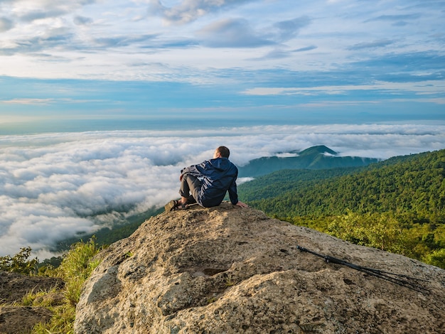 Trekker sitting on the mountain with beautiful sunrise and sea of mist in the morning on khao luang mountain in ramkhamhaeng national park,sukhothai province