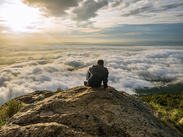スコータイ県ラムカムヘン国立公園のカオルアン山の朝、美しい日の出と霧の海と山に座っているトレッカー