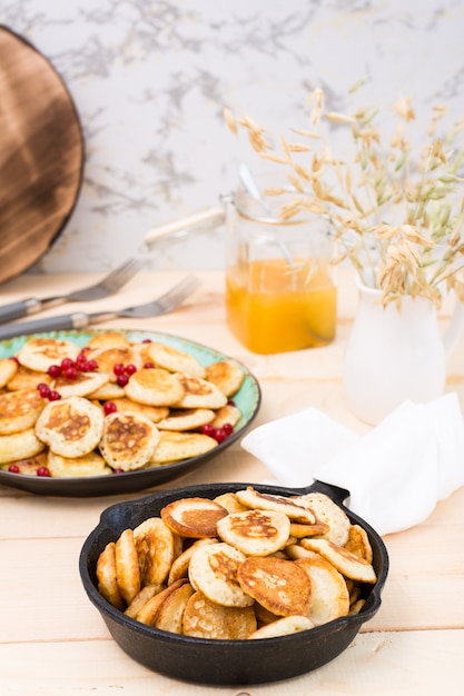 Trend ontbijt. Nederlandse mini pannenkoeken in een pan en op een bord met rode aalbessen op een houten tafel.