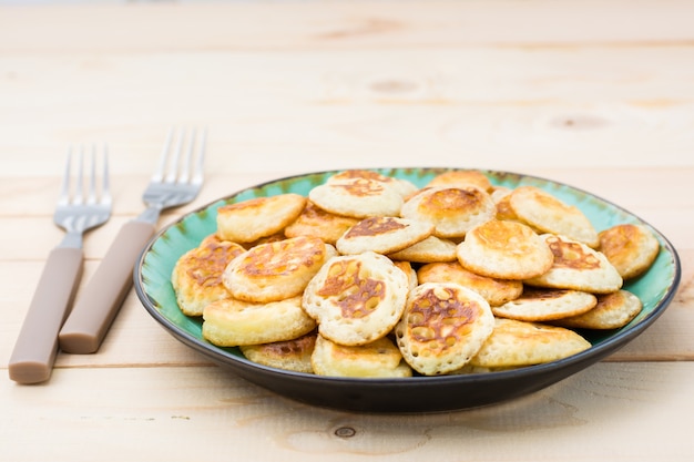 Foto trend ontbijt. nederlandse mini pannenkoeken op plaat en twee vorken op een houten tafel.