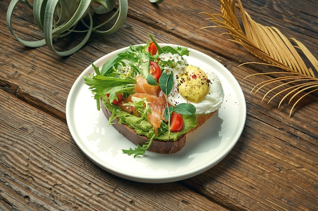 Trend street food - avocado toast with guacamole, poached egg and salmon in a plate on a wooden table