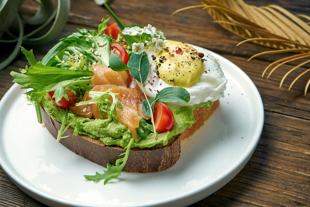 Trend street food - avocado toast with guacamole, poached egg and salmon in a plate on a wooden