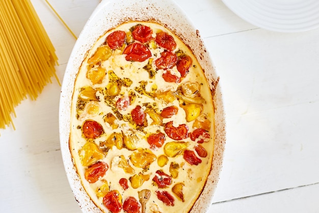 Trending viral recipe of baked tomatoes and feta with pasta, Fetapasta on a white wooden background. New, popular dinner dish, Top view, copy space.