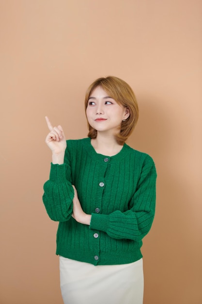 Trendy aantrekkelijke jonge vrouw die zich voordeed over een beige achtergrond die met de vinger wijst en naar haar rechts kijkt