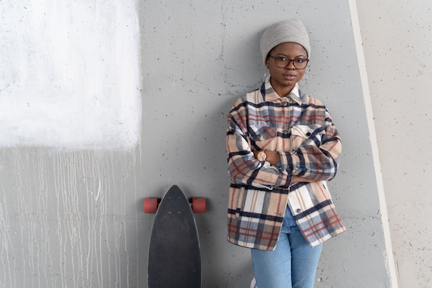 Trendy african female with skateboard young black woman standing at concrete wall with arms folded