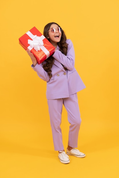 trendy amazed curious kid in sunglasses and suit hold gift box full length, amazement.