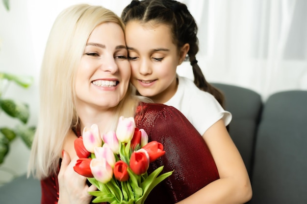 Trendy attractive cheerful mother and daughter enjoying holiday together having big flawless seasonal colorful bouquet of tulips, comfort pleasure joy enjoyment concept on grey background