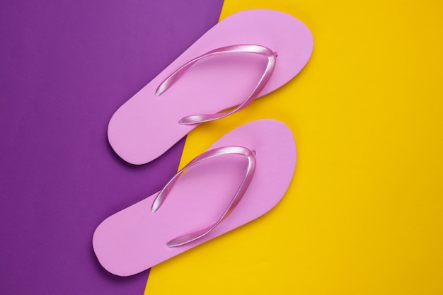 Trendy beach pink flip flops on purple yellow paper background. Top view