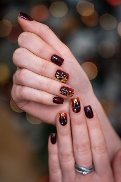 Trendy and beautiful manicure on female hands. nails crimson or Burgundy in combination with gold gloss.