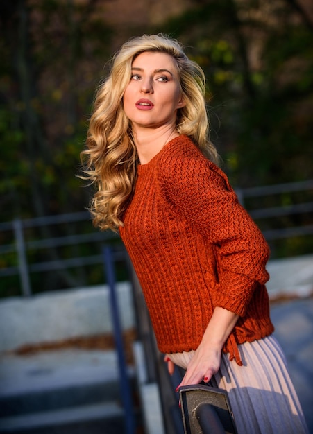 Trendy beauty autumn woman curly hair outdoor girl long blond hair city walk girl in corrugated skirt and sweater Pleated trend haidresser and makeup fall fashion season female beauty