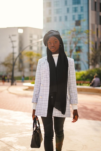 Photo trendy black woman in headscarf carrying bag in park