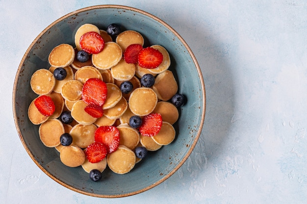 Trendy breakfast with mini pancakes, blueberries and strawberries, top view.