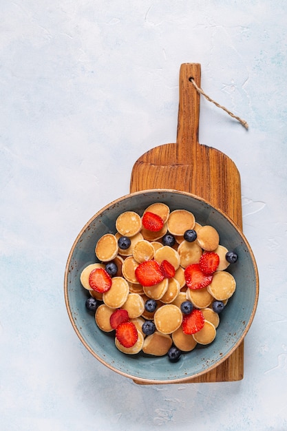 Trendy breakfast with mini pancakes, blueberries and strawberries, top view.