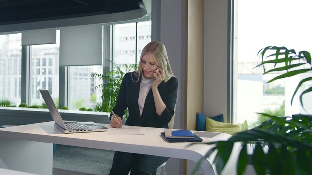 Trendy business woman watching laptop and speaking on phone