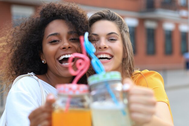 Модные крутые хипстерские девушки, друзья пьют коктейль на фоне городского города.