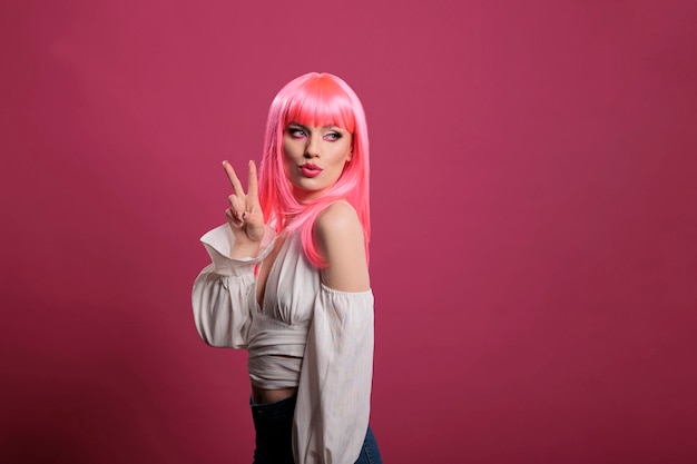 Trendy coole vrouw met roze haar die vredesteken en kusgezicht voor de camera doet. zorgeloos aantrekkelijk meisje met overwinningssymbool en vreedzaam gebaar met twee vingers omhoog in de studio.