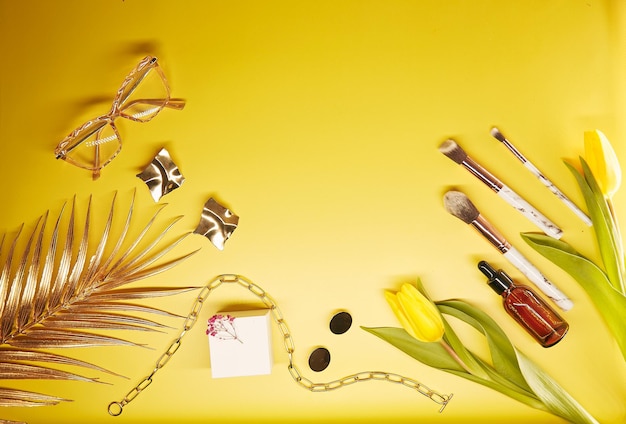 Foto accessori cosmetici alla moda spazzole per il trucco e accessori su sfondo giallo scatola mockup tulipani bicchieri siero decorazioni contagocce e spazio per la copia foto di alta qualità