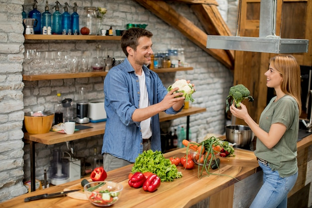 Trendy couple peeling and cutting vegetables from the market in rustic kitchen