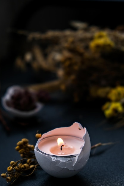 trendy easter decorations. cracked organic eggs with dry grass and dry flowers candle light on plate. bird feather. copy space. greeting card. dark background.