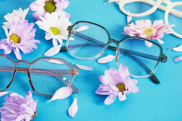 Trendy eyeglasses and flowers on blue background