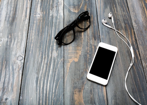 Trendy eyeglasses and smartphone on wooden background