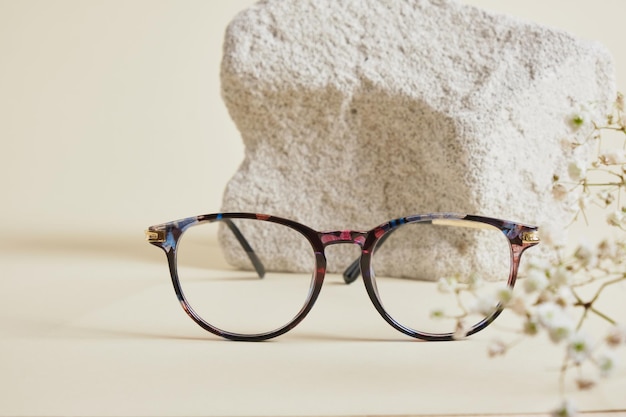 Trendy fashion eyeglasses on concrete podium and Gypsophila flowers on beige background