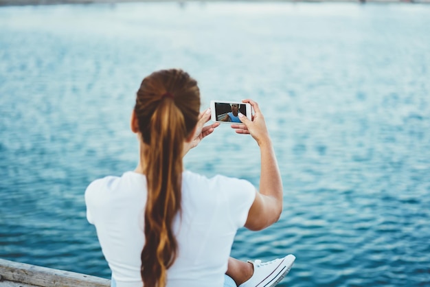 携帯電話を手に持って携帯電話のカメラを見て自分の写真を撮るトレンディな女性