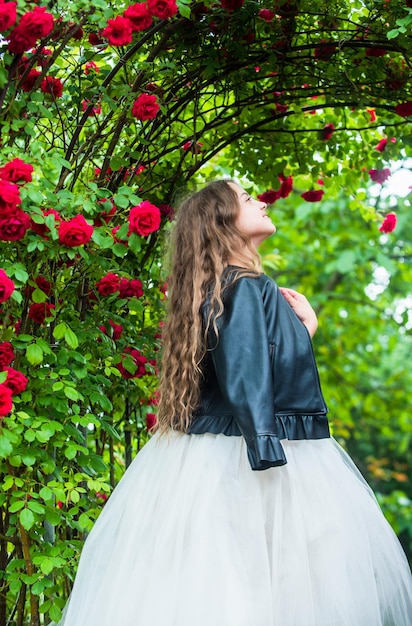 Trendy girl fancy dress and leather jacket in roses garden modern princess concept