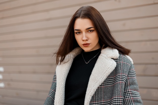 Trendy girl in fashion clothes near a wooden wall