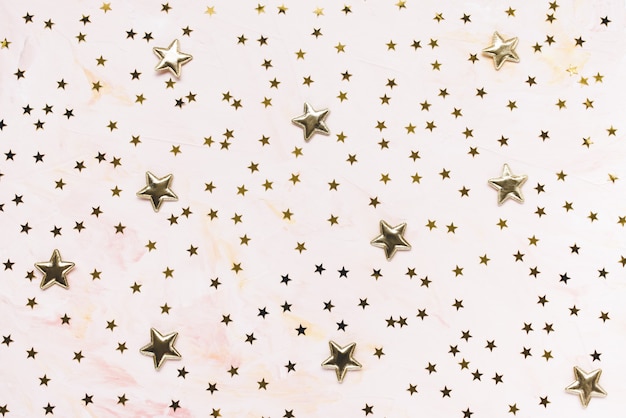 Trendy golden foil confetti stars on pink background.