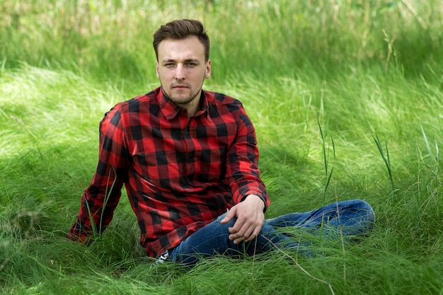 Trendy guy is smiling and  resting on the grass