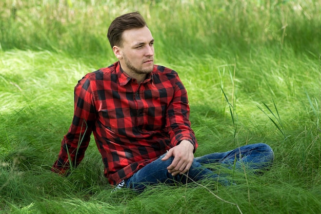 Trendy guy is smiling and  resting on the grass