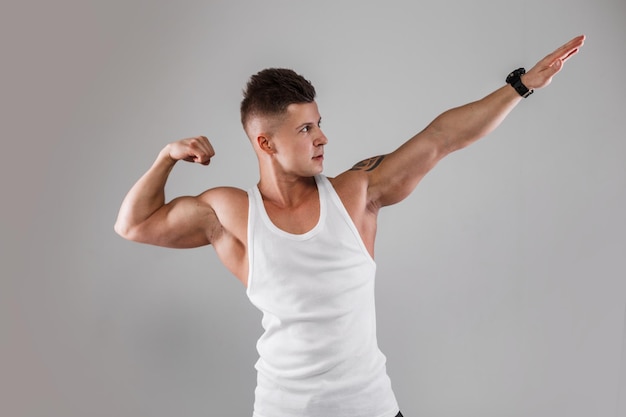 Trendy handsome athletic man with a muscular sporty healthy body wearing a white mock up tank top poses in the studio on a gray background