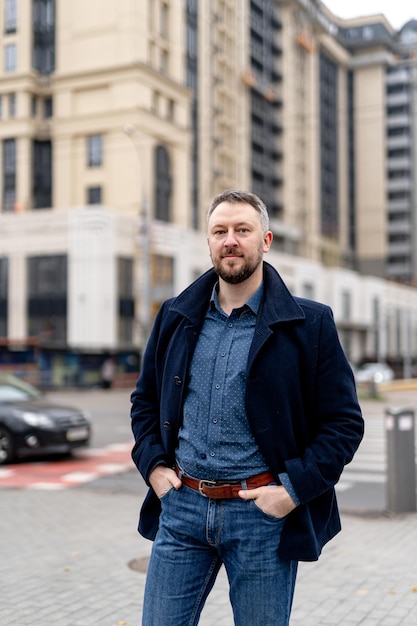 Trendy handsome man in gray coat and dark suit. Autumn city blurred background.