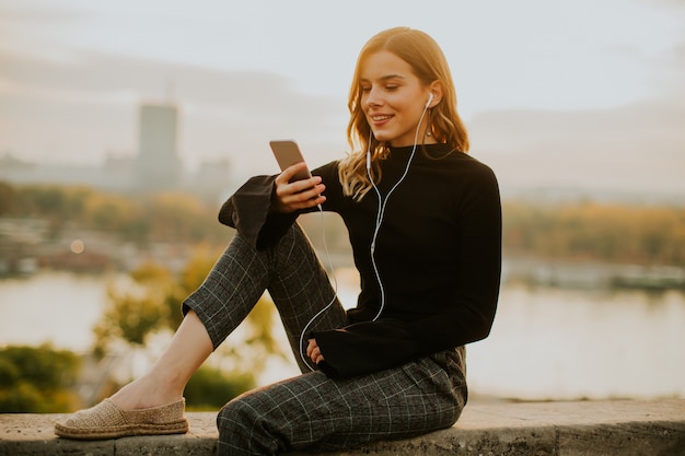 Trendy jonge vrouw het luisteren muziek van smartphone openlucht bij zonsondergang