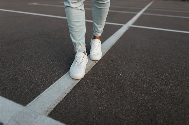 Trendy jongeman in vintage witte lederen sneakers in modieuze blauwe denim broek. stijlvolle zomerschoenen voor heren. casual ontwerp. close-up van mannelijke benen.