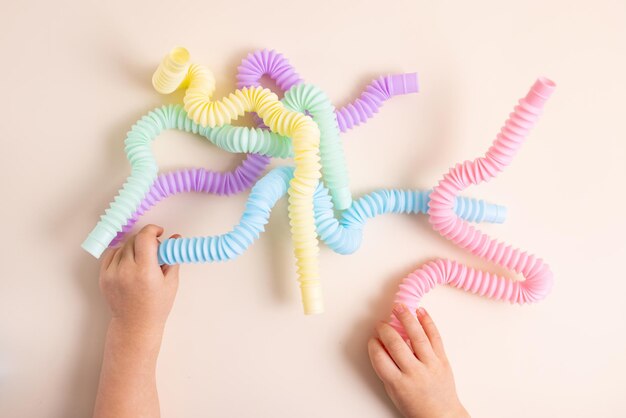 Trendy kids toys pastel colorful poptube in baby toddler hands on beige background set of forms and ...